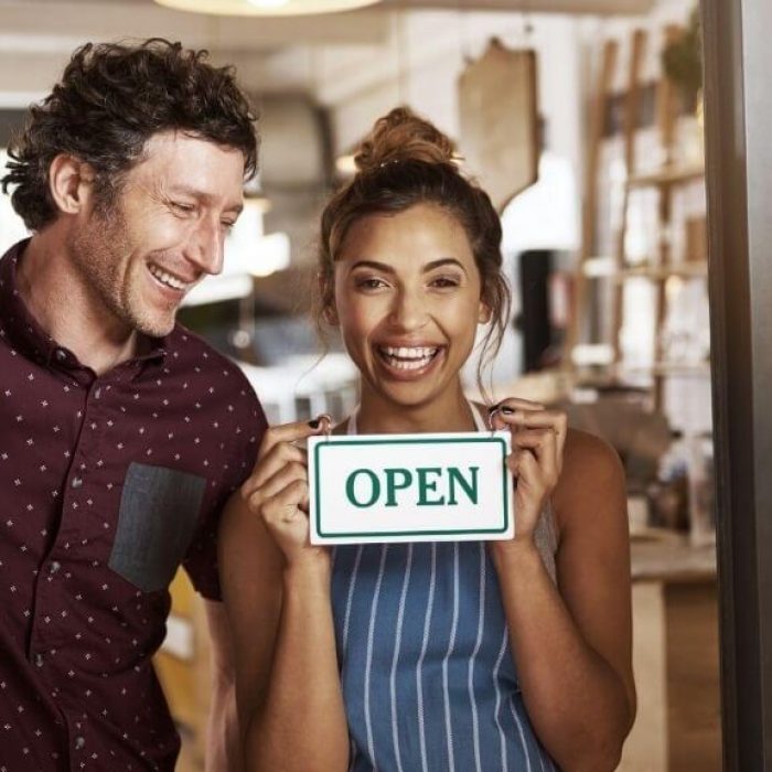 man and woman in front of business door holding an open sign